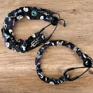 May include: Two black stethoscope covers with a colorful print of sea creatures and a trident. The covers are made of fabric and have a stretchy design.
