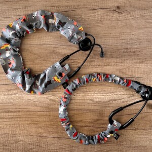 May include: Two stethoscope covers with a gray background and a colorful pattern of dogs. The covers are made of fabric and have a stretchy design.