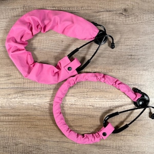 May include: Two pink stethoscope covers with black stethoscopes. The covers are made of a soft, stretchy fabric and have a button closure.