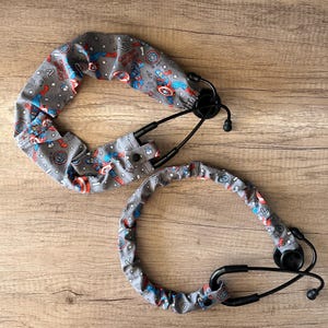 May include: Two stethoscopes with gray covers featuring a Captain America pattern. The covers have a repeating design of Captain America, shields, and stars in red, blue, and white. The stethoscopes are black.