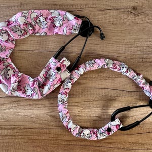 May include: Two black stethoscopes with pink and white fabric covers featuring a cartoon cat design.