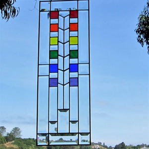 May include: A rectangular stained glass panel featuring a vertical central column of square glass tiles in red, orange, yellow, green, blue, and purple. The panel is framed in black metal and consists of clear glass sections surrounding the colorful center.