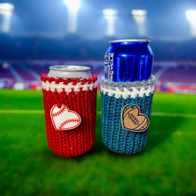 Op de afbeelding: Twee gebreide blikjeskoelers, &eacute;&eacute;n rood met een honkbalhart, de andere blauwgroen met een voetbalhart. De koelers staan op een groen veld met een stadionachtergrond. De rode koeler heeft de tekst "Supports Digestive Health".