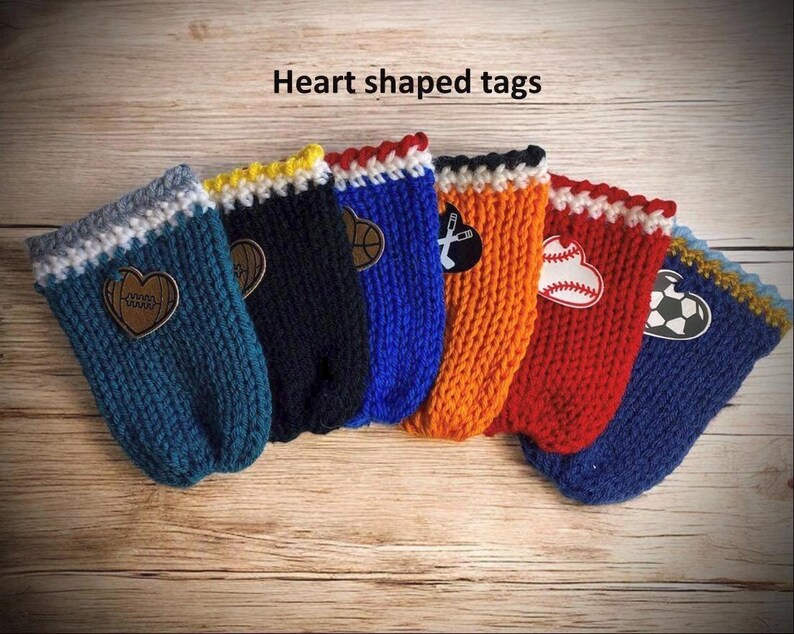 Op de afbeelding: Een verzameling hartvormige labels in verschillende kleuren, waaronder teal, marineblauw, blauw, oranje en rood. Elk label heeft een ander sportthema, zoals een basketbal, honkbal en voetbal. De labels zijn gebreid en hebben een decoratieve rand.