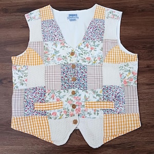 May include: A patchwork vest with a variety of floral, gingham, and knit fabric patches. The vest features wooden buttons and a V-neck design. The color palette includes white, yellow, pink, and blue.