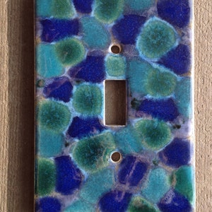 May include: A light switch cover with a blue and green mosaic pattern. The cover is made of ceramic and has a glossy finish.