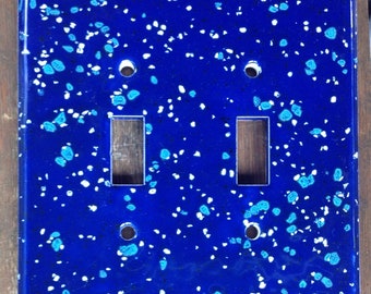 May include: A blue light switch cover with white and turquoise speckles. The cover has two toggle switches.