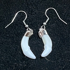 May include: A pair of silver earrings with white tooth-shaped charms. The earrings have a simple hook design.