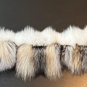 May include: A long strip of white and gray fox fur. The fur is soft and fluffy, and it is arranged in a series of overlapping sections.