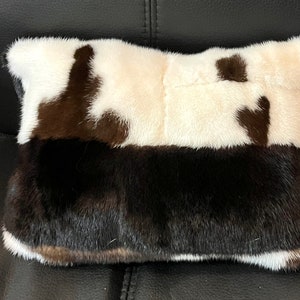May include: A rectangular pillow with a brown and white fur pattern. The pillow is made of two different types of fur, one is white with brown patches and the other is brown with white patches.
