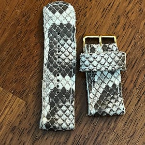 May include: A white and gray snakeskin watch band with a gold buckle.