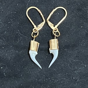 May include: A pair of gold earrings with white claw-shaped charms. The earrings have a hook closure.