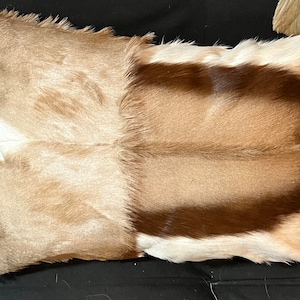 May include: A brown and white fur pillow with a long, shaggy texture. The pillow is made from real animal fur and has a natural, rustic look.