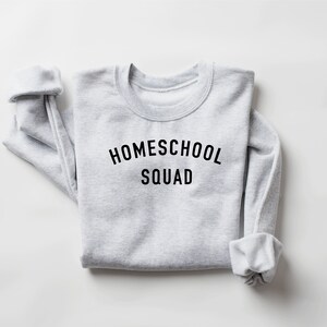 Puede incluir: Una sudadera gris con el texto "HOMESCHOOL SQUAD" impreso en negro.