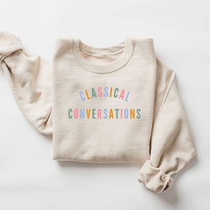 May include: A beige sweatshirt with the text "CLASSICAL CONVERSATIONS" printed in rainbow colors.