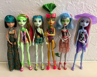 May include: Six Monster High dolls are displayed, each with unique features. They have various skin tones, hair colors, and outfits. The dolls are wearing swimsuits, dresses, and accessories. The dolls are standing in a row against a white background.