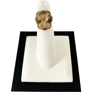May include: A silver ring with a carved cameo stone featuring a woman's profile. The cameo is set in a silver frame with a decorative design.