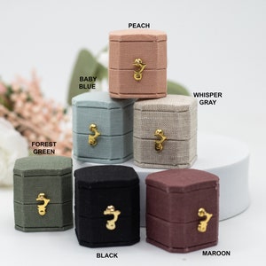 Puede incluir: Surtido de cajas de anillos hexagonales en varios colores, incluyendo melocotón, azul bebé, gris susurro, verde bosque, negro y granate. Cada caja tiene un cierre dorado.