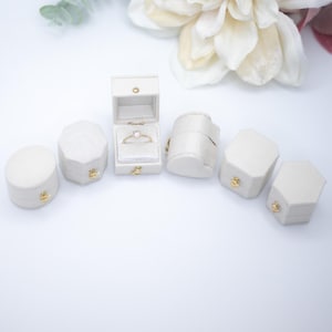 May include: Six white ring boxes with a gold latch. One box is open and contains a gold ring with a single diamond.