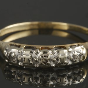 May include: A gold band ring with a row of five small diamonds set in a white metal. The ring is a classic design and would make a beautiful gift.