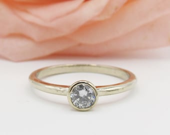 May include: A simple silver band ring with a bezel set round brilliant cut diamond.