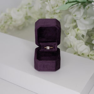 May include: A purple velvet ring box with a gold ring inside. The ring has a single, clear diamond.