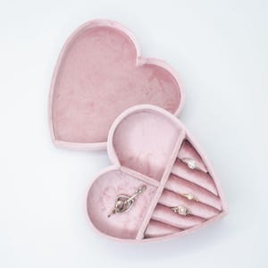 May include: A pink velvet heart-shaped jewelry box with a hinged lid. The box has multiple compartments for storing rings and a larger compartment for a necklace or other jewelry.