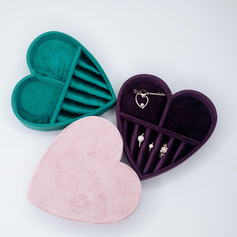 May include: Three heart-shaped velvet jewelry boxes in pink, green, and purple. The boxes have compartments for rings and earrings.