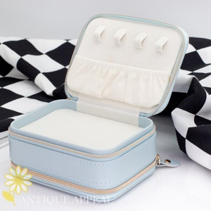 Pode incluir: Um estojo de viagem para joias azul claro com fecho de correr e interior branco. O estojo tem um pequeno bolso e v&aacute;rias ranhuras para an&eacute;is.