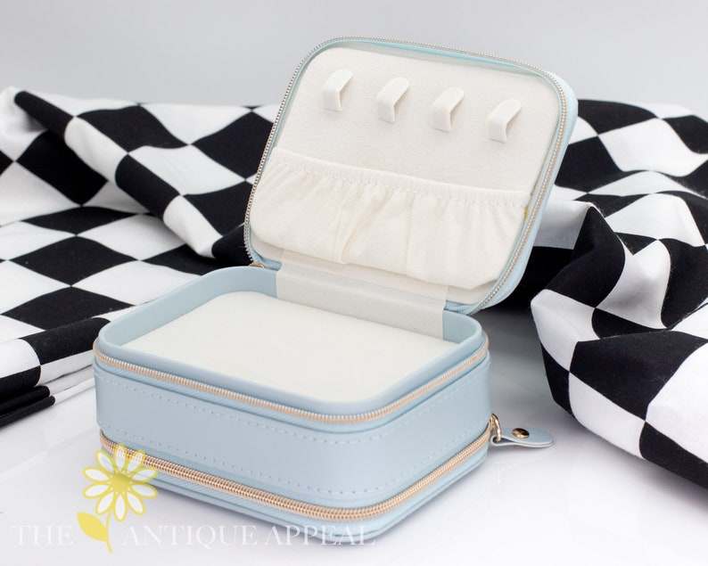 Pode incluir: Um estojo de viagem para joias azul claro com fecho de correr e interior branco. O estojo tem um pequeno bolso e v&aacute;rias ranhuras para an&eacute;is.