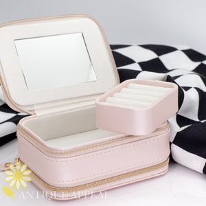 Pode incluir: Uma caixa de joias de imita&ccedil;&atilde;o de couro rosa com um espelho e um porta-an&eacute;is remov&iacute;vel. A caixa tem um z&iacute;per dourado e um amuleto de margarida dourado.
