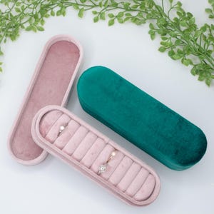 May include: Two velvet ring boxes, one pink and one green, with a pink box open showing a ring holder with three rings.