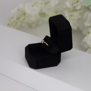 May include: A black velvet ring box with a gold ring with a diamond setting inside.