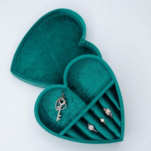 May include: A teal velvet heart-shaped jewelry box with a key charm and four ring slots.
