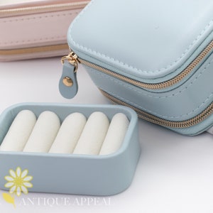 Pode incluir: Uma caixa de joias de viagem azul claro com fecho de correr e um inserto para an&eacute;is. A caixa &eacute; feita de couro sint&eacute;tico e tem um fecho de correr dourado.