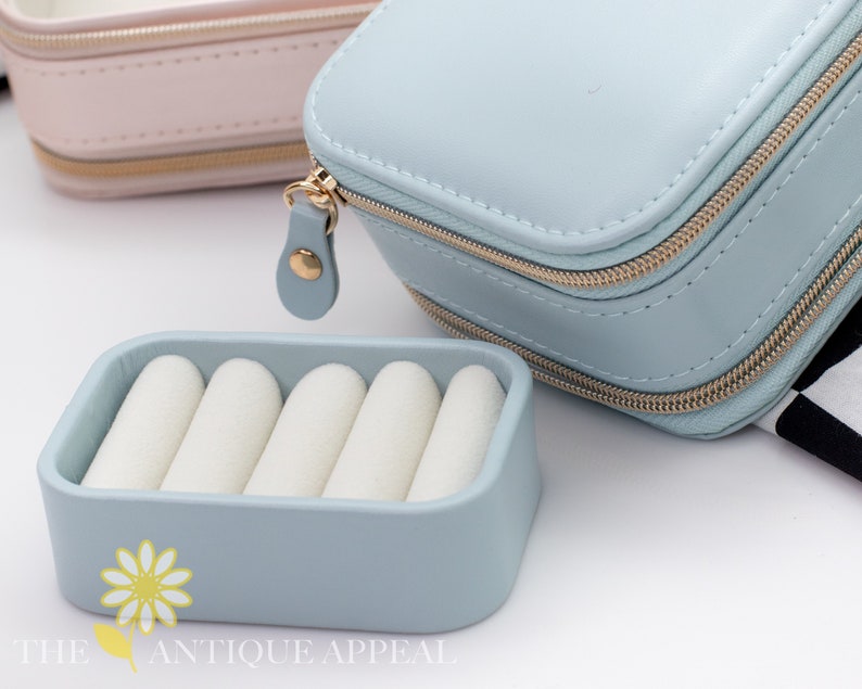 Pode incluir: Uma caixa de joias de viagem azul claro com fecho de correr e um inserto para an&eacute;is. A caixa &eacute; feita de couro sint&eacute;tico e tem um fecho de correr dourado.