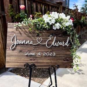 Dark Wooden sign with a couples’s 2 first names connected with a heart in white 3D lettering and wedding date.