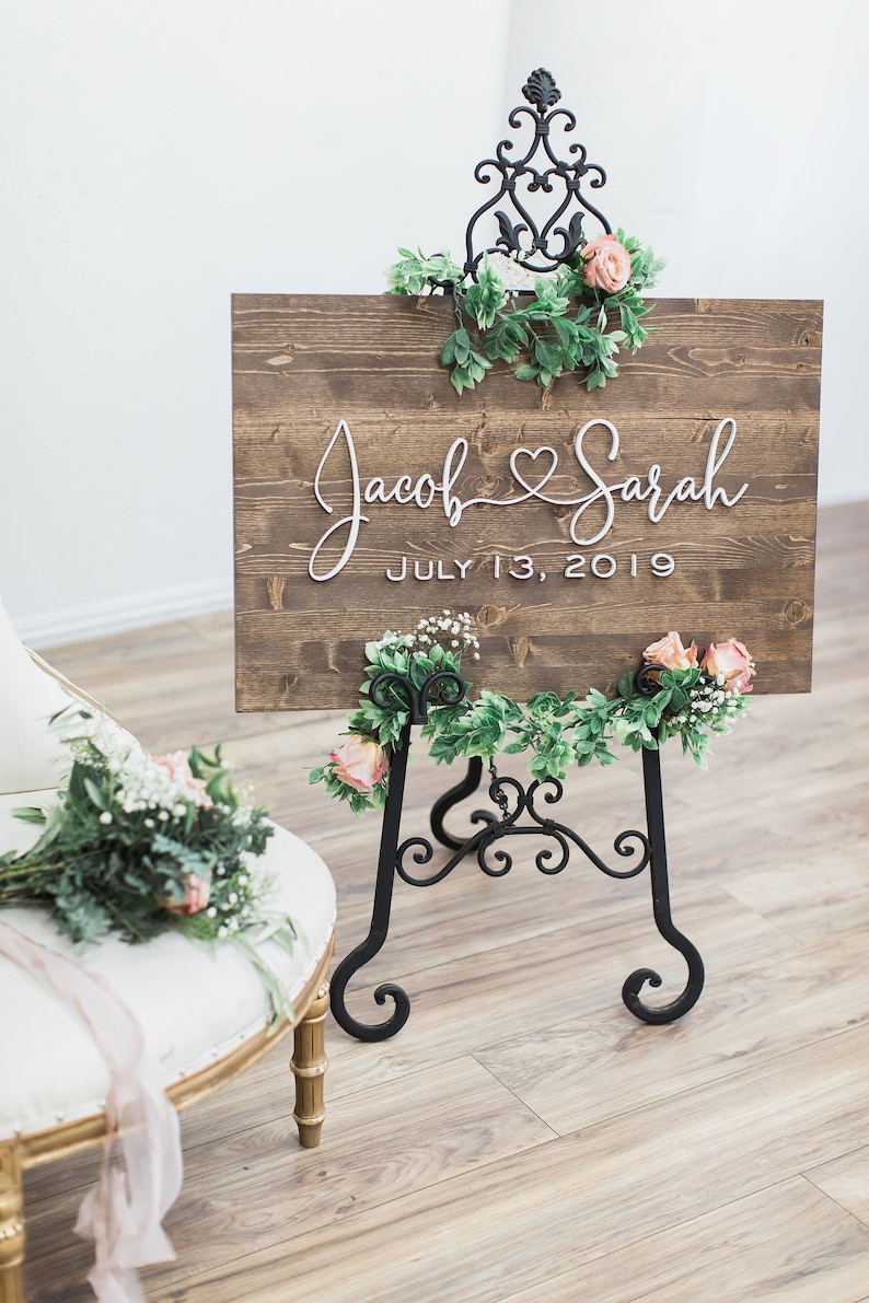 Custom Wood Wedding Sign personalized with couple's first names connected with a heart and a wedding date below. Walnut stained wood with white 3D letters.