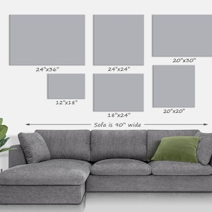 May include: A display of six gray rectangular wall art pieces of varying sizes, including 24"x36", 24"x24", 20"x30", 12"x18", 20"x20", and 18"x24". A gray sectional sofa with a green pillow is below the art. The sofa is 90" wide.