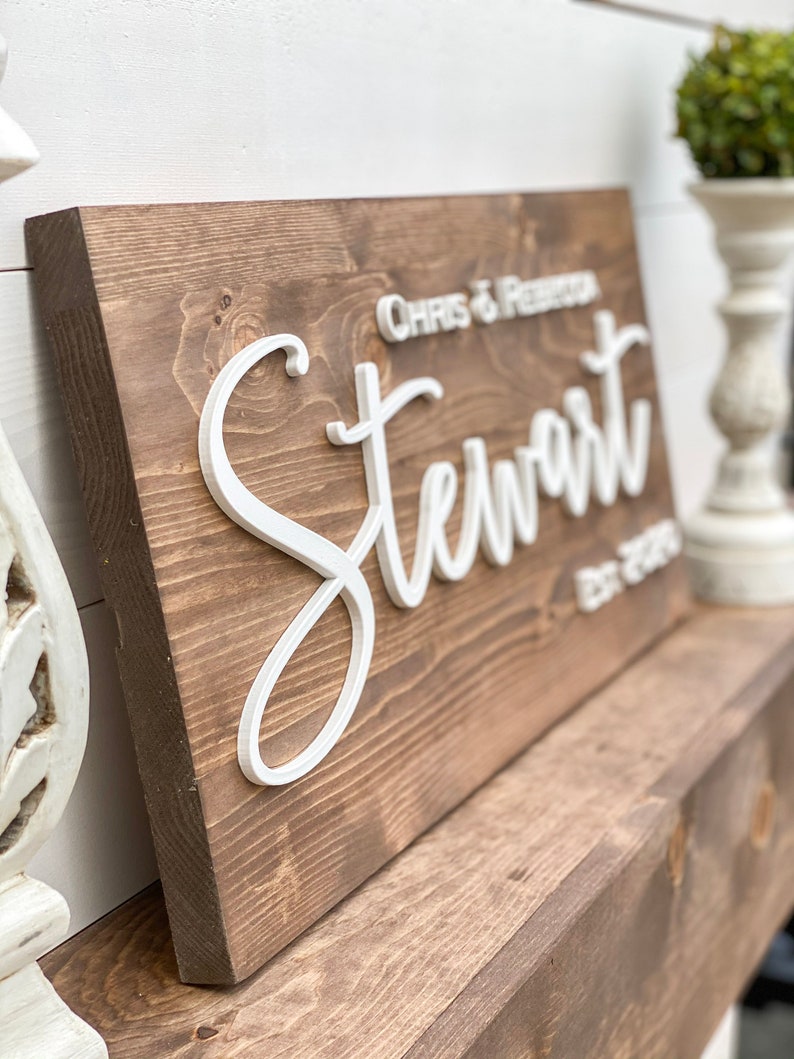 May include: A wooden sign with the text "Chris &  Preston Stewart est. 2023" in white raised letters.