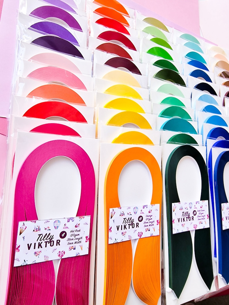 Puede incluir: Surtido de tiras de papel de colores para manualidades, dispuestas en filas sobre un fondo rosa. Cada tira est&aacute; etiquetada con el nombre de la marca "Tilly Viktor" y un n&uacute;mero. Las tiras son de varios colores, incluyendo rosa intenso, naranja, verde y azul.