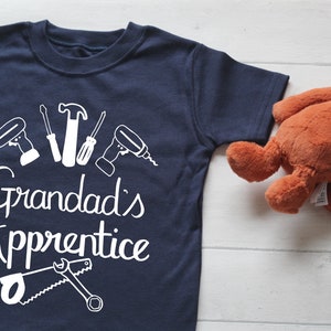 May include: A navy blue t-shirt with a white graphic of tools and the text "Granddad's Apprentice".