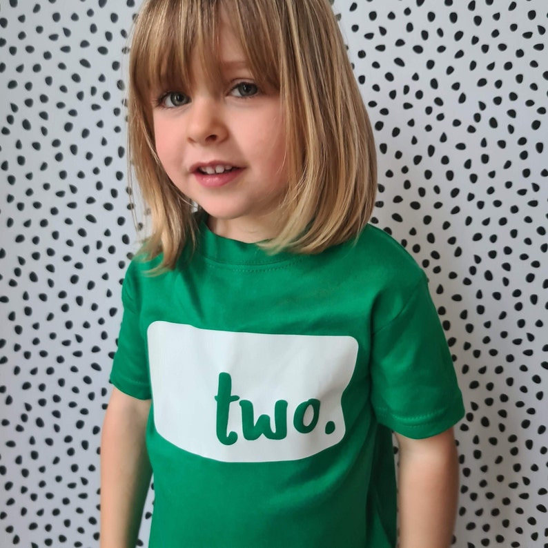 Little girl wearing green t-shirt with 'Two' logo printed in white.