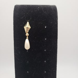 May include: A gold earring with a teardrop-shaped pearl dangling from a geometric gold charm.