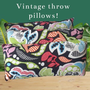 Op de afbeelding: Drie vintage sierkussens met een zwarte achtergrond en kleurrijke bloemen- en vogelpatronen. De kussens hebben rode, groene, blauwe en witte ontwerpen. De tekst "Vintage throw pillows!" staat bovenaan.