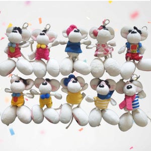 Könnte beinhalten: Eine Sammlung von Plüschmaus-Spielzeugen mit weißen Körpern, großen Ohren und verschiedenen Outfits. Jede Maus hat einen Schlüsselanhänger. Zu den Outfits gehören rosa, blaue, gelbe und gestreifte Hemden und Kleider. Die Mäuse haben schwarz-weiße Gesichter.