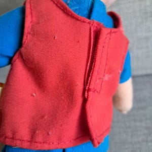 Puede incluir: Primer plano de un chaleco rojo sobre una camisa azul. El chaleco est&aacute; hecho de una tela texturizada y tiene costuras visibles. La camisa azul es visible en el cuello y las mangas. La imagen est&aacute; bien iluminada, mostrando los detalles de la ropa.