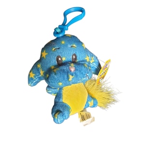 Op de afbeelding: Een blauwe pluche hond met gele sterpatronen en een gele buik. Het speelgoed heeft een blauwe clip en een gele staart. Het speelgoed heeft een label.