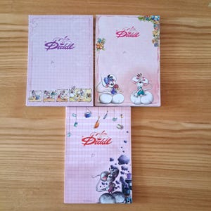 May include: Three rectangular paper notepads featuring the Diddl mouse character. Each notepad has a light pink background with grid lines or floral accents, displaying the Diddl logo and various illustrations of the cartoon mouse character.