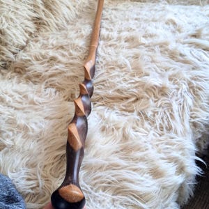 Peut inclure: Une longue canne en bois dotée d'un manche et d'un fût sculptés en spirale. Le bois présente un contraste bicolore avec des sections alternées brun clair et brun foncé, affichant une finition lisse et polie sur toute sa longueur.